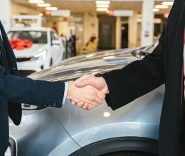 Close up of Men Shaking Hands at a car dealership with new Cars in Background